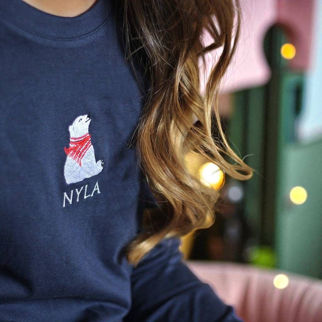 Person wearing a navy blue shirt with a polar bear logo and 'NYLA' text, blurred background with lights.