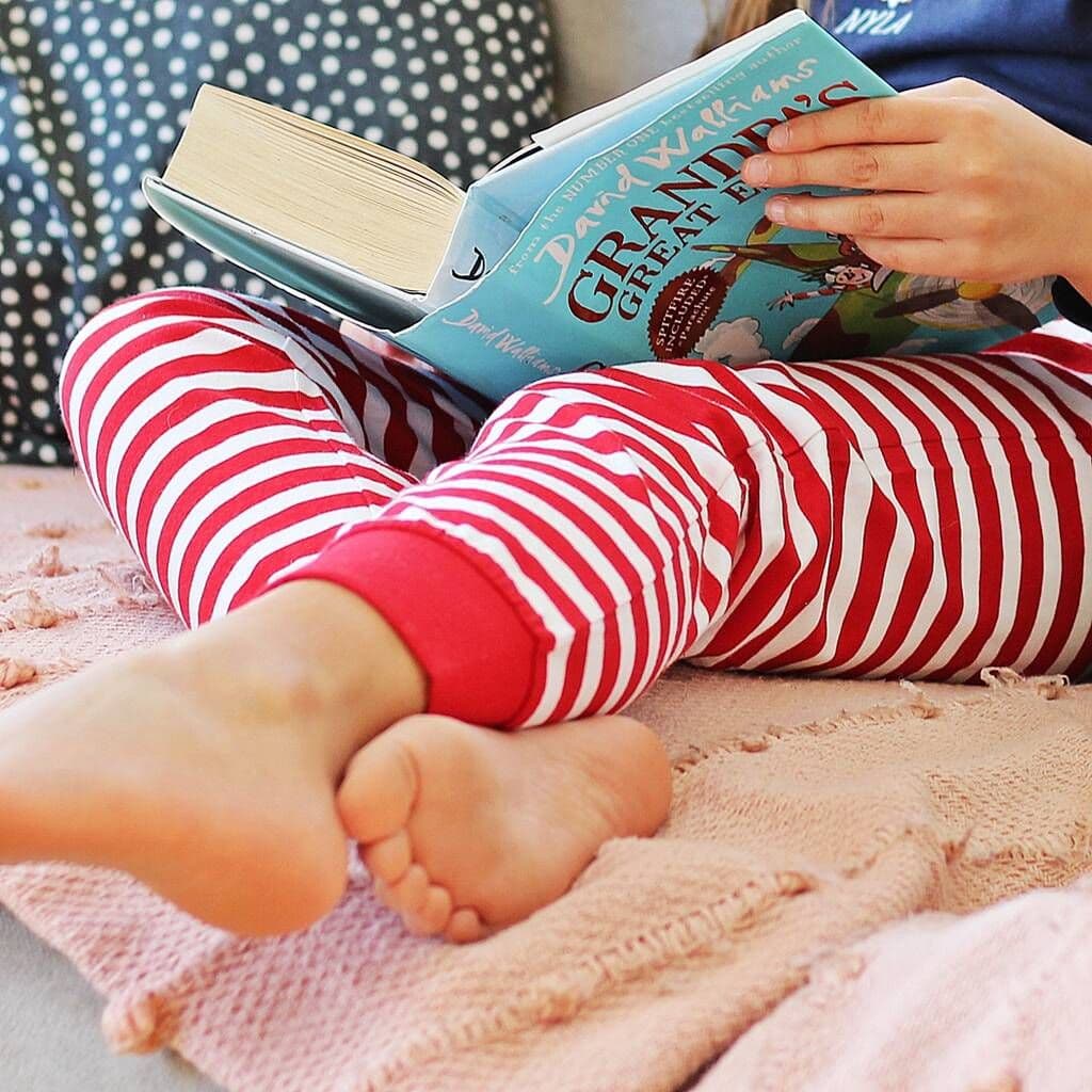 Child's legs in red and white striped pants holding a book titled 'Grandpa's Great Escape' on a pink blanket.