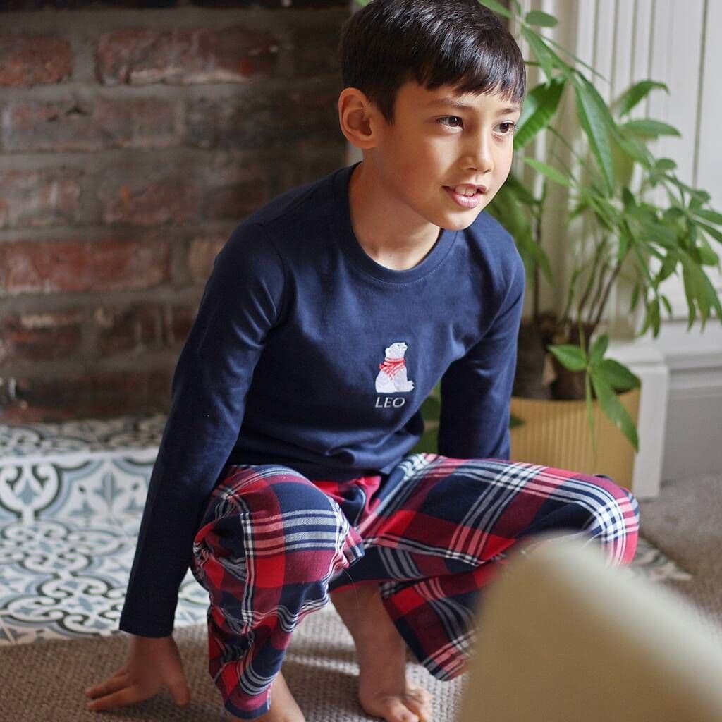 Child wearing a navy blue shirt with a logo and red plaid pants sitting on the floor.