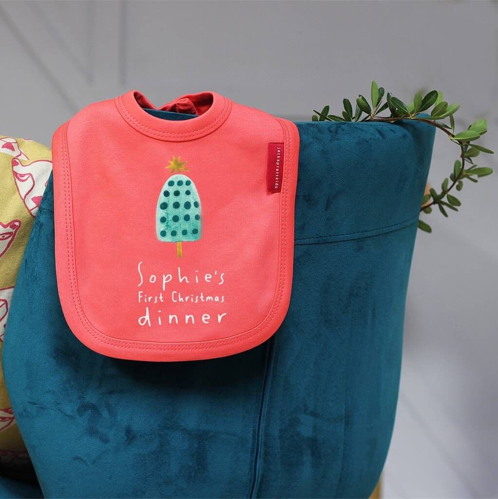 Pink bib with 'Sophie's First Christmas Dinner' text on a blue bag.