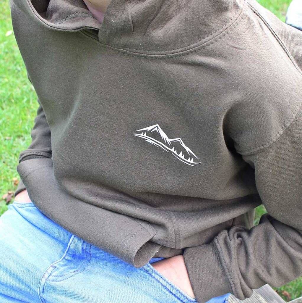 Person wearing a brown hoodie with a mountain logo on a grassy background
