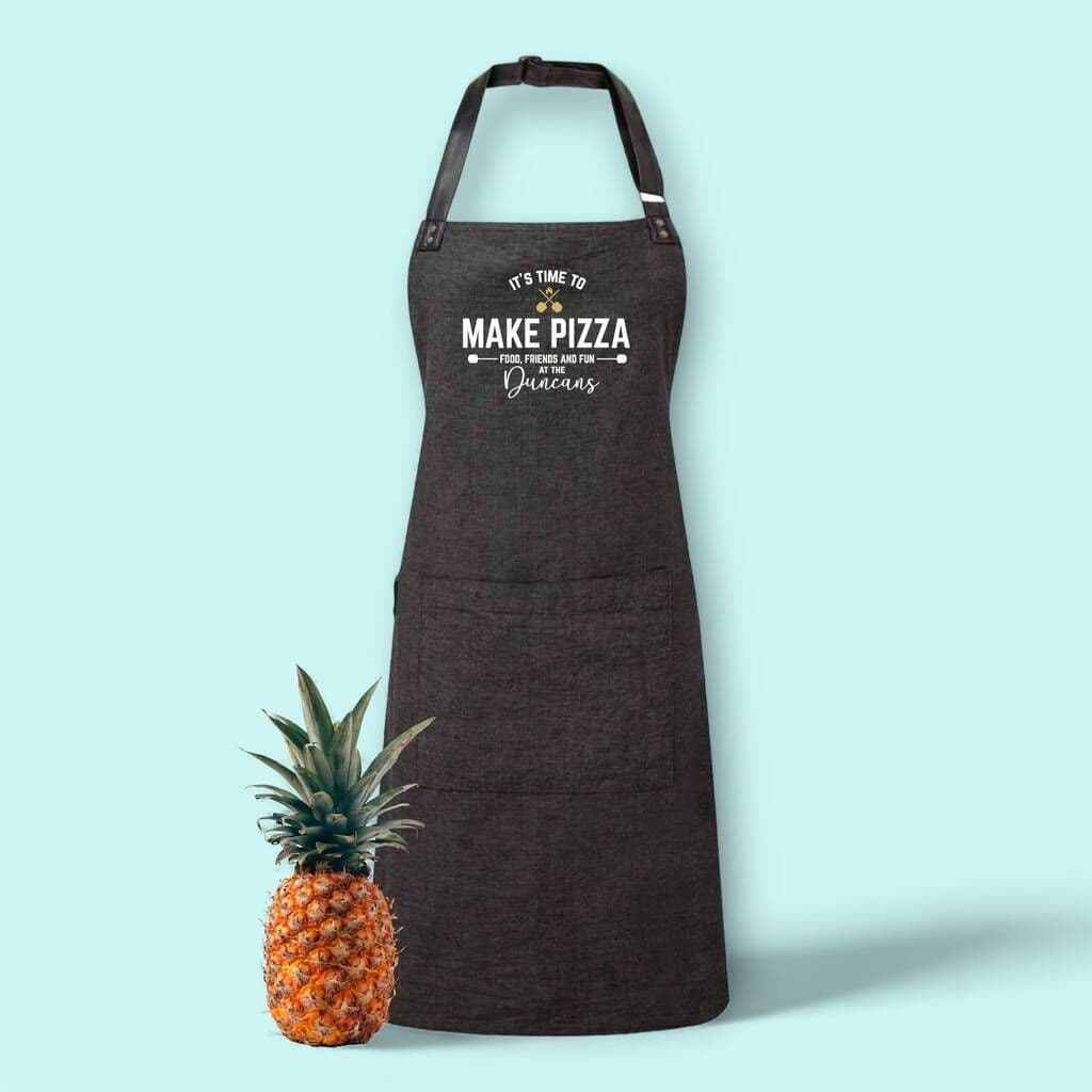 Black apron with text next to a pineapple on a light blue background
