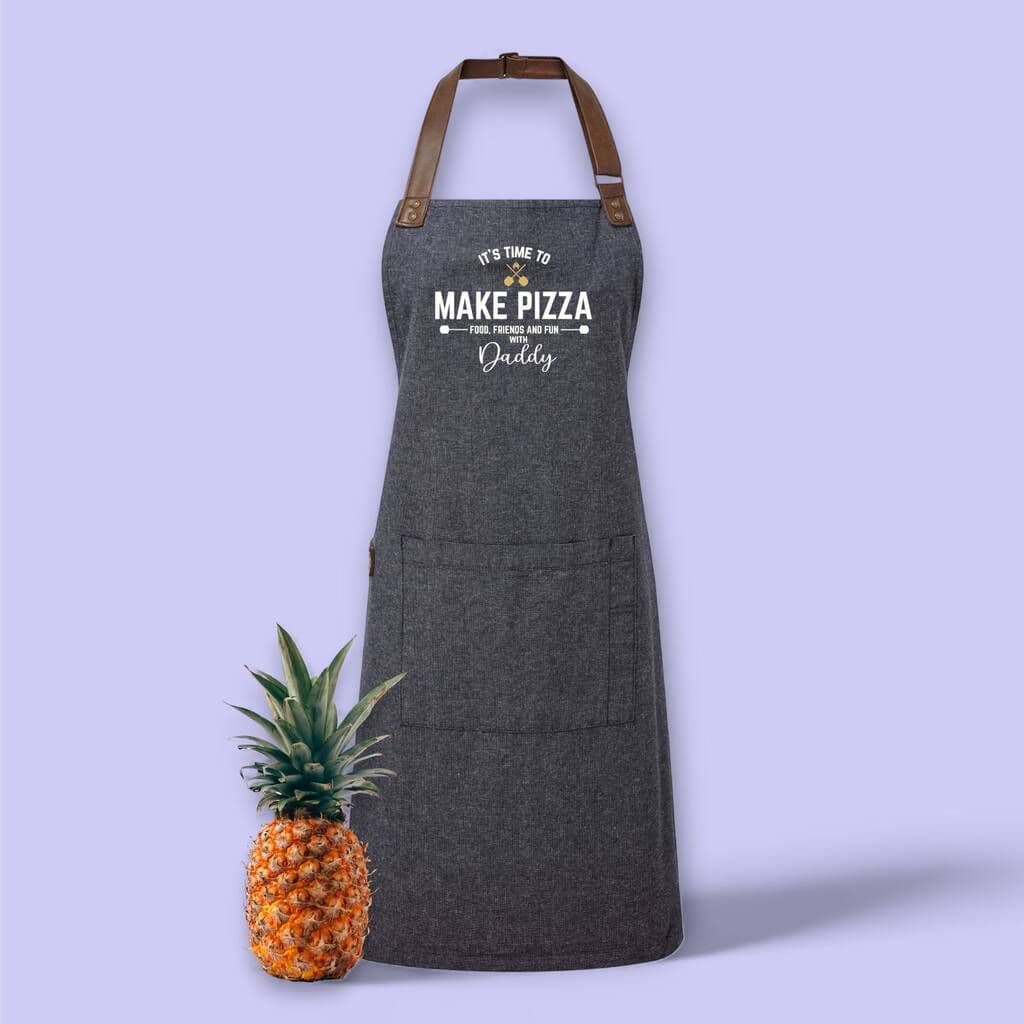 Gray apron with text next to a pineapple on a light purple background
