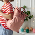 Blush pink lifestyle (Bella) — Child holding personalised blush pink recycled roll top backpack with white embroidered name Bella