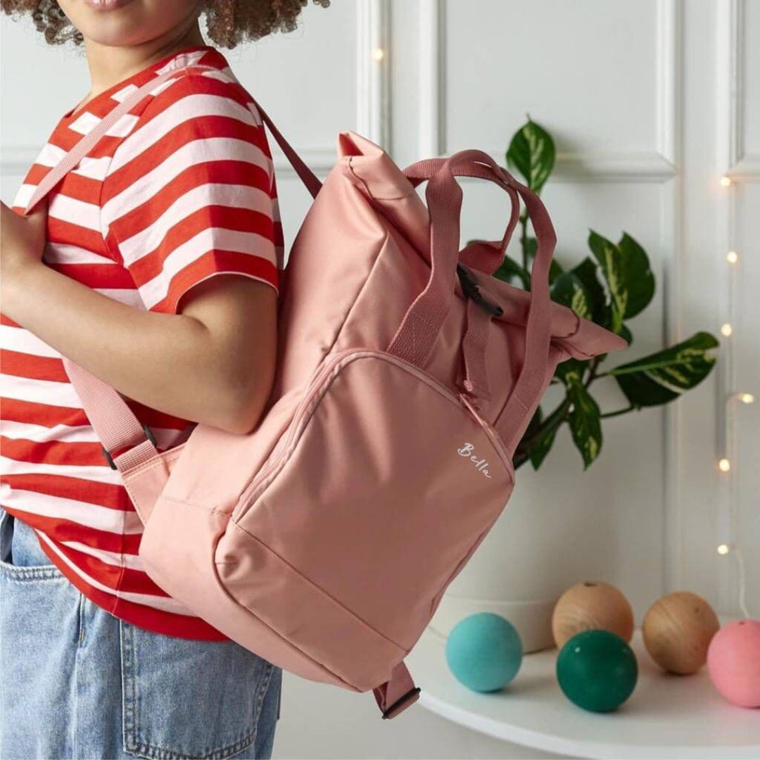 Blush pink lifestyle (Bella) — Child holding personalised blush pink recycled roll top backpack with white embroidered name Bella