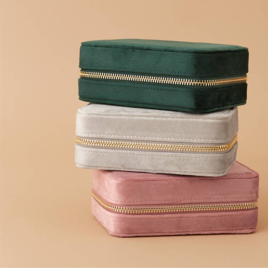 Three stacked jewelry boxes in green, gray, and pink with gold zippers on a beige background.