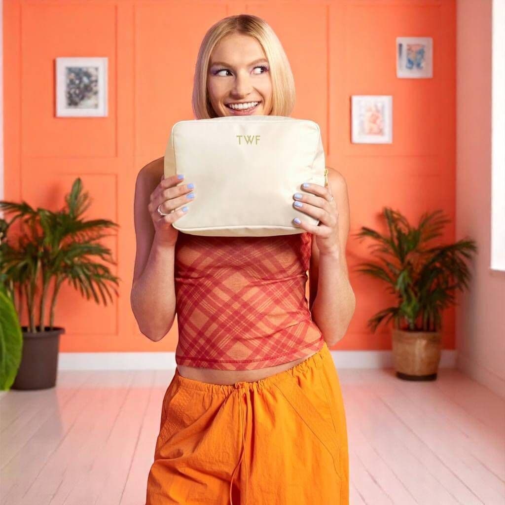 Person holding a beige pillow with 'TWF' on it in a room with orange walls and plants.