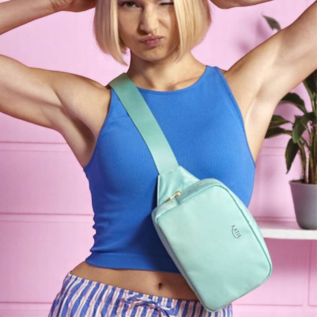 Woman wearing a blue top and striped shorts with a light blue crossbody bag against a pink background.