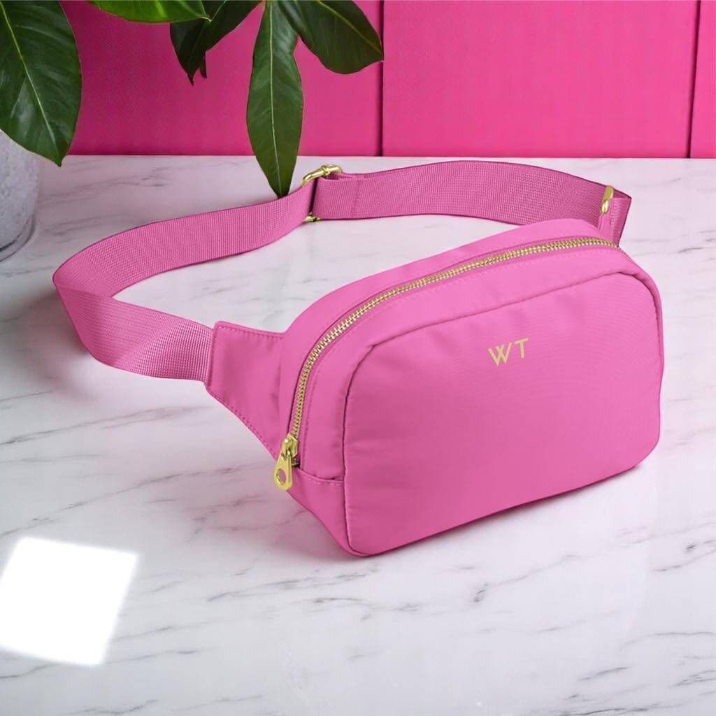 Pink waist bag with gold zippers on a marble surface with a pink background