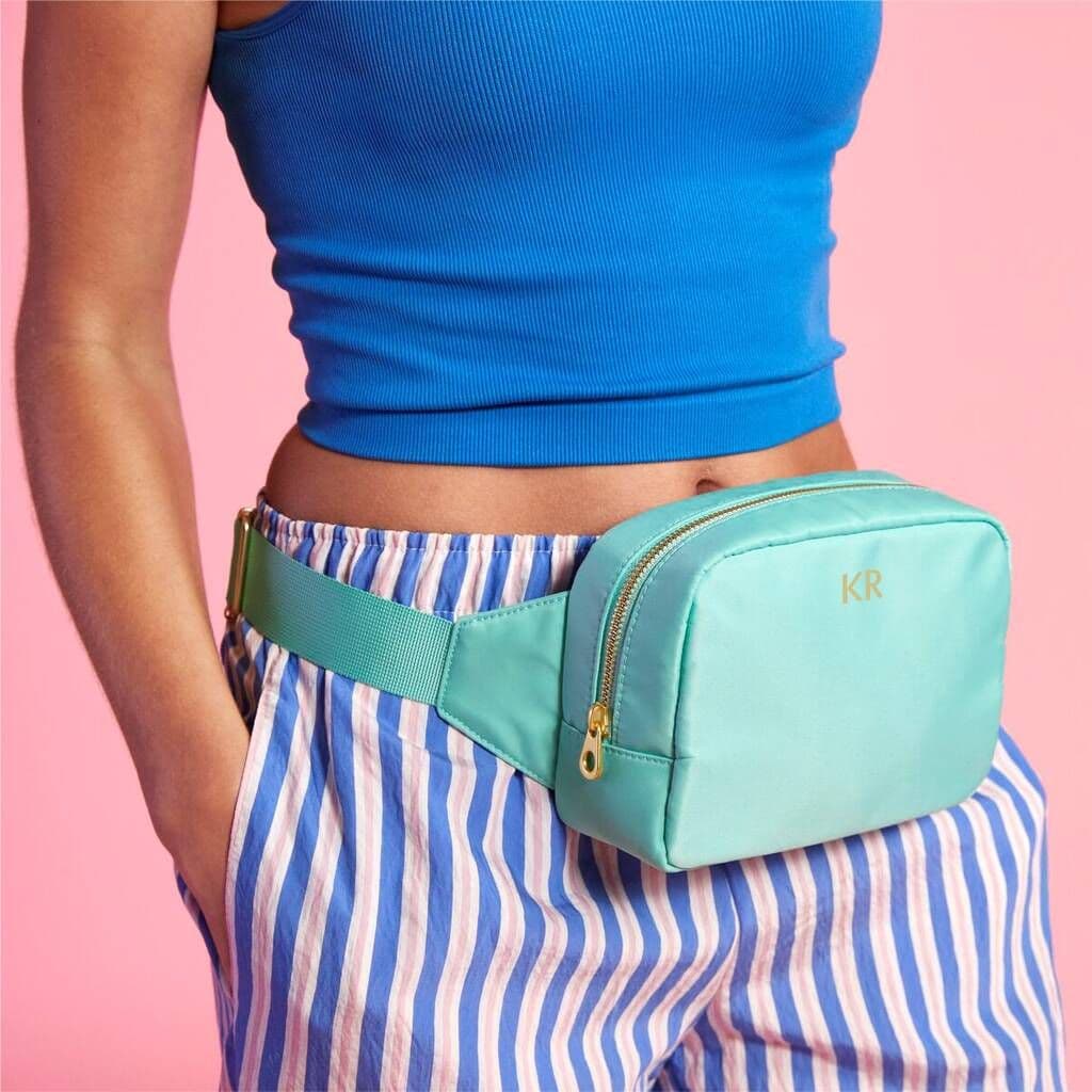 Person wearing a turquoise fanny pack with a pink background