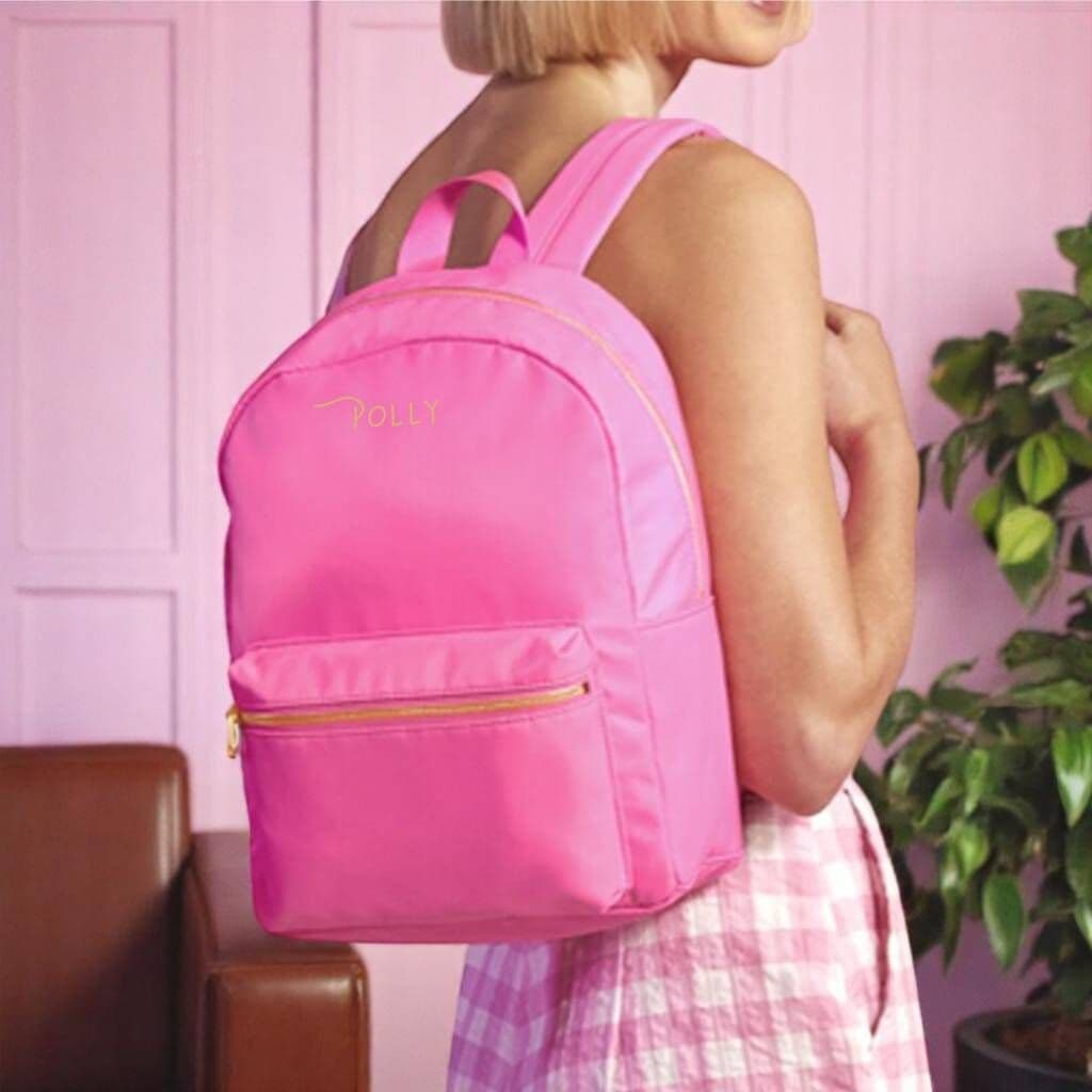 Person wearing a pink backpack with 'Folly' branding against a pink wall.