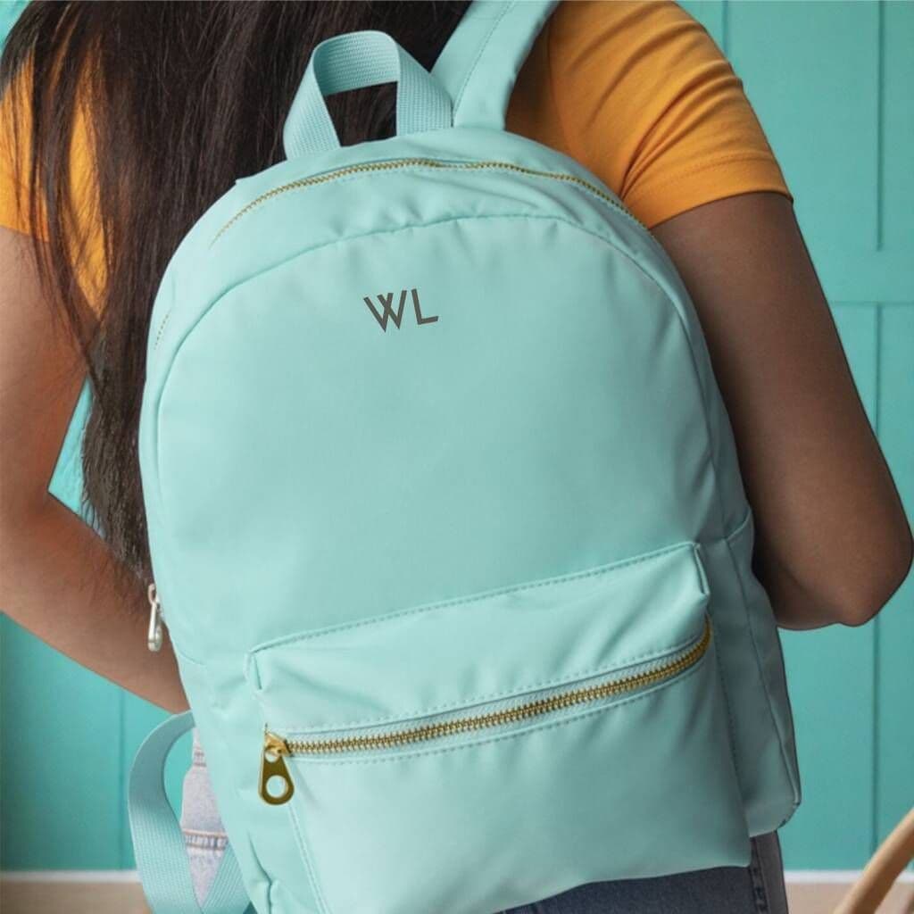 Person wearing a light blue backpack with 'WL' initials against a teal background