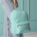 Mint green backpack with 'Katie' branding held by a person against a teal wall.