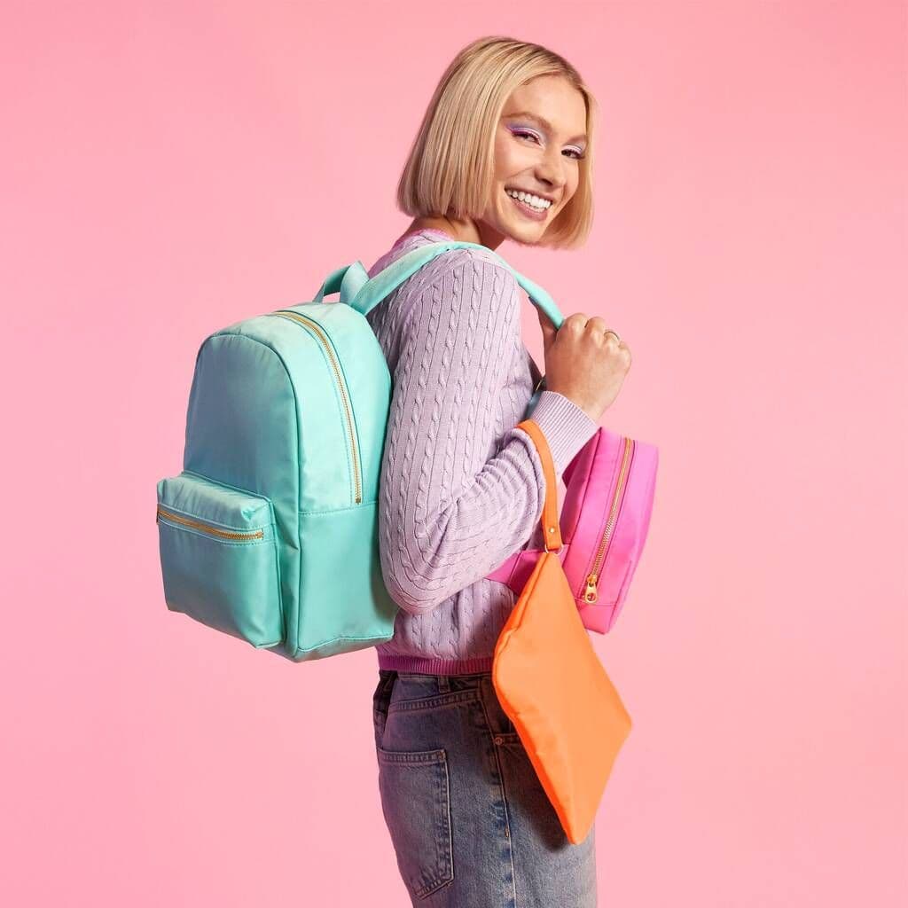Woman with colorful backpacks against a pink background