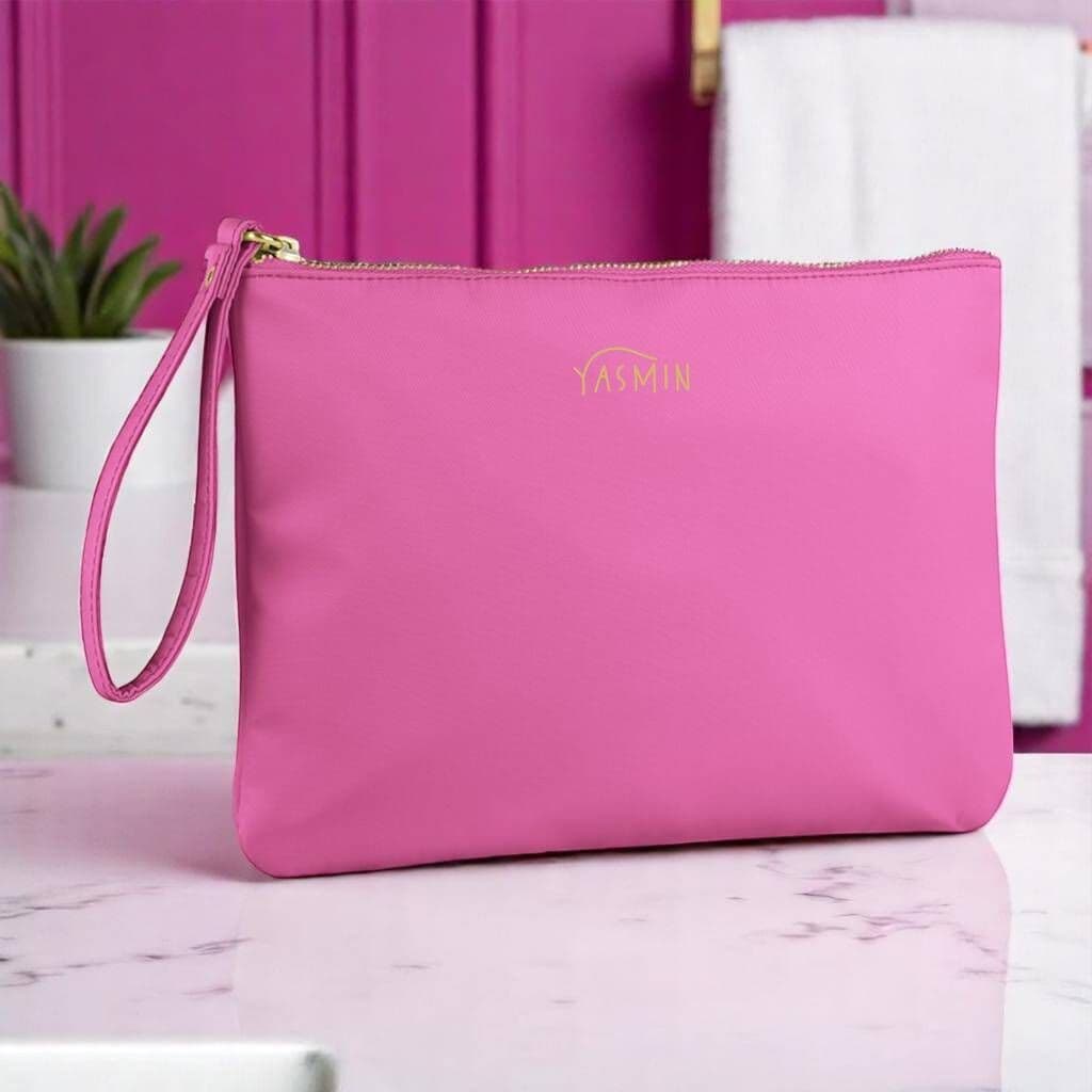 Pink pouch with a gold zipper and 'YASMIN' branding on a pink surface.