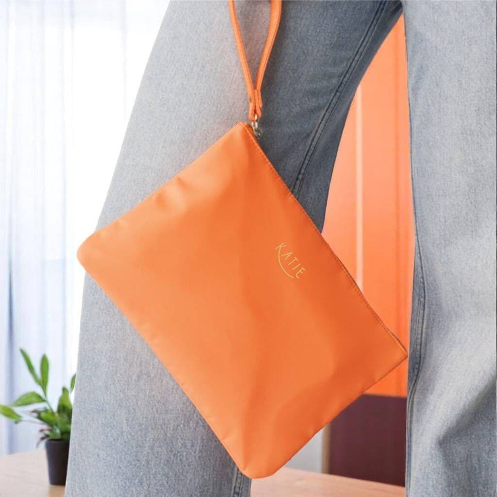 Orange pouch with 'Katie' branding held by a person, blurred background