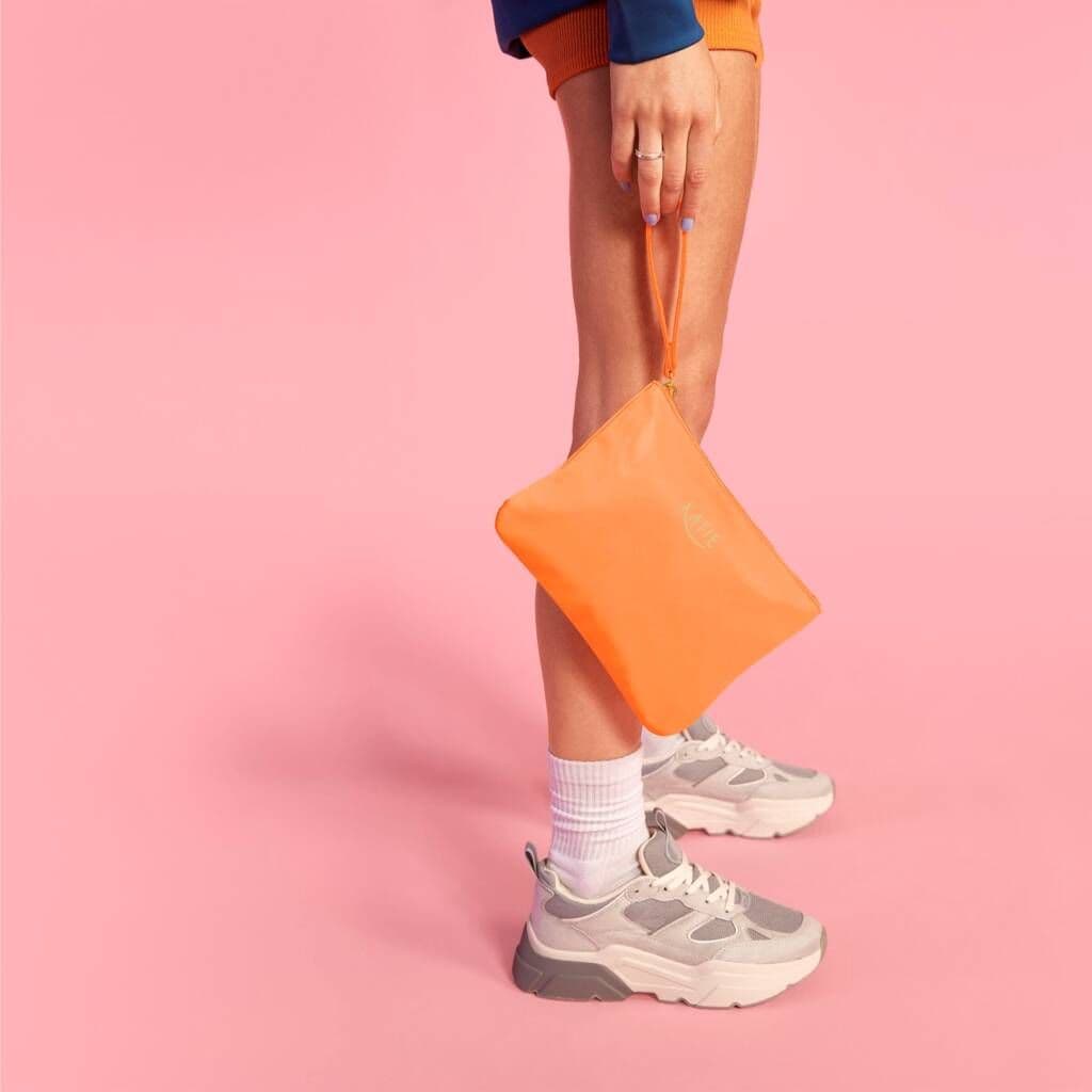 Person holding an orange pouch with a pink background