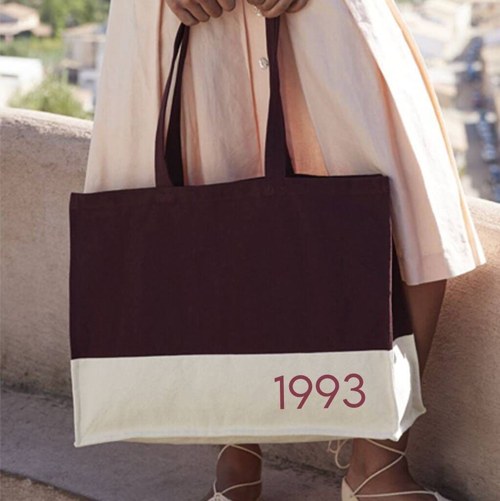 Person holding a tote bag with '1993' printed on it, outdoors.