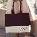 Person holding a tote bag with '1993' printed on it, outdoors.