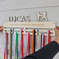 Wooden belt display with colorful ribbons and engraved text, held by two hands against a light gray background.