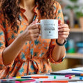Person holding a mug with 'Teacher - Educational Rockstar' text in an indoor setting.