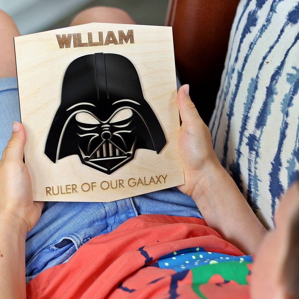 Child holding a wooden plaque with Darth Vader design and 'William, Ruler of Our Galaxy' text.