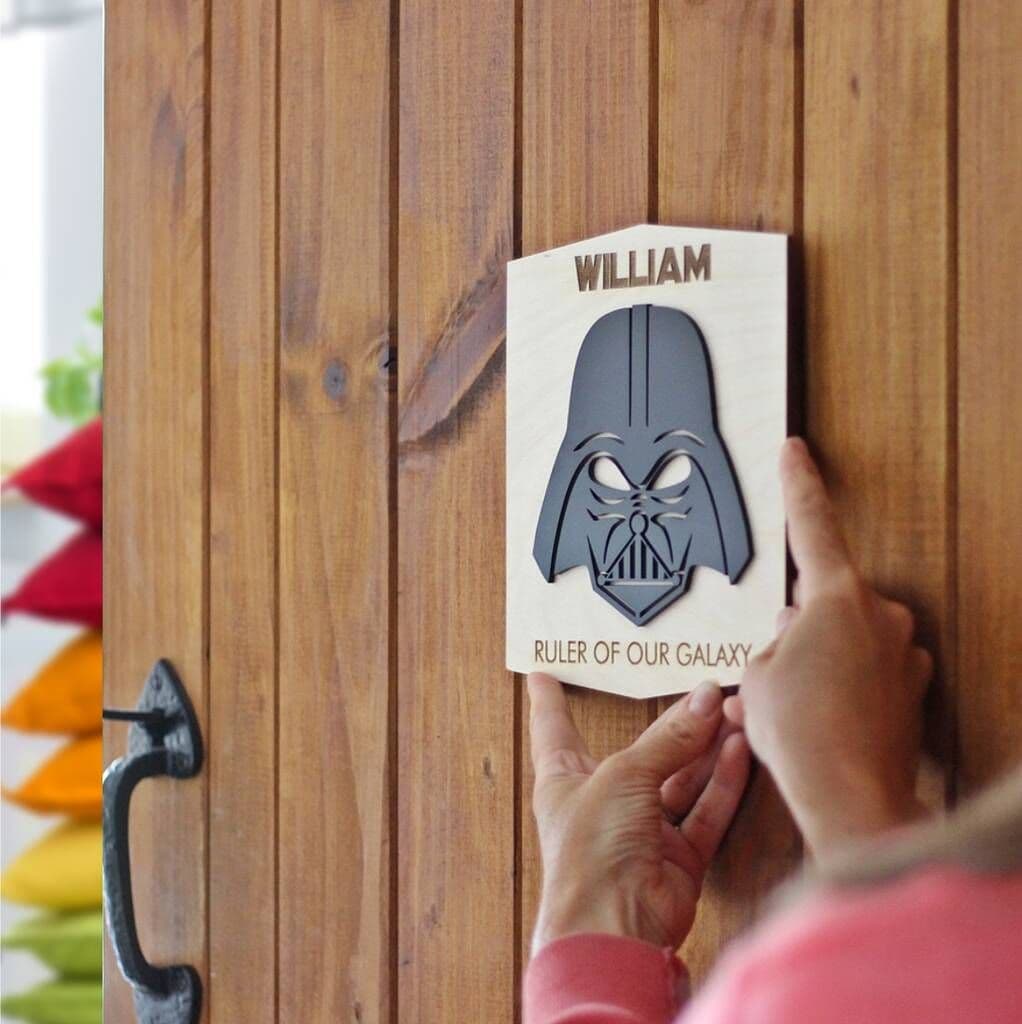 Person holding a wooden plaque with Darth Vader design and text on a wooden surface