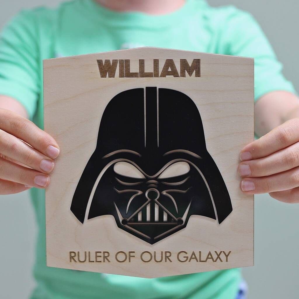 Person holding a wooden plaque with Darth Vader helmet design and text 'William, Ruler of Our Galaxy'.