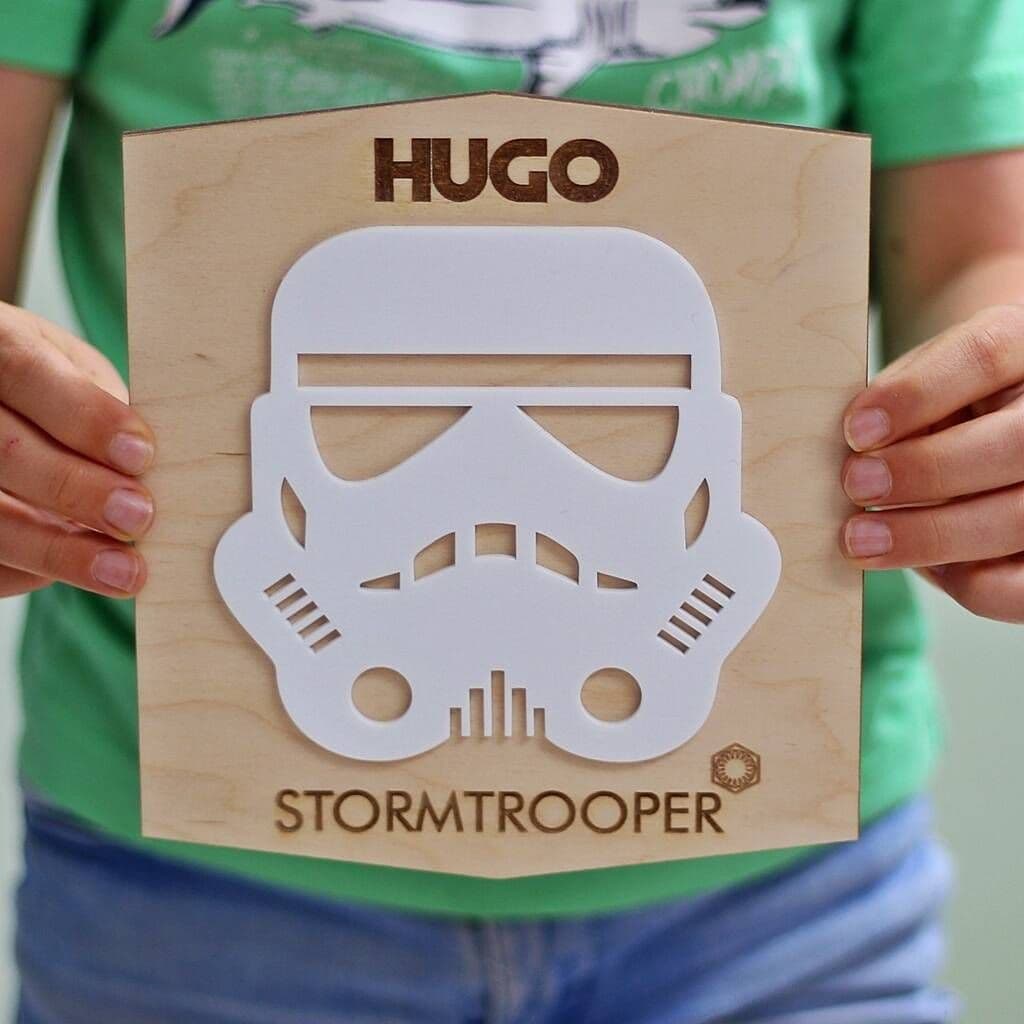 Wooden cutout of a stormtrooper helmet with 'Hugo' and 'Stormtrooper' text, held by a person.